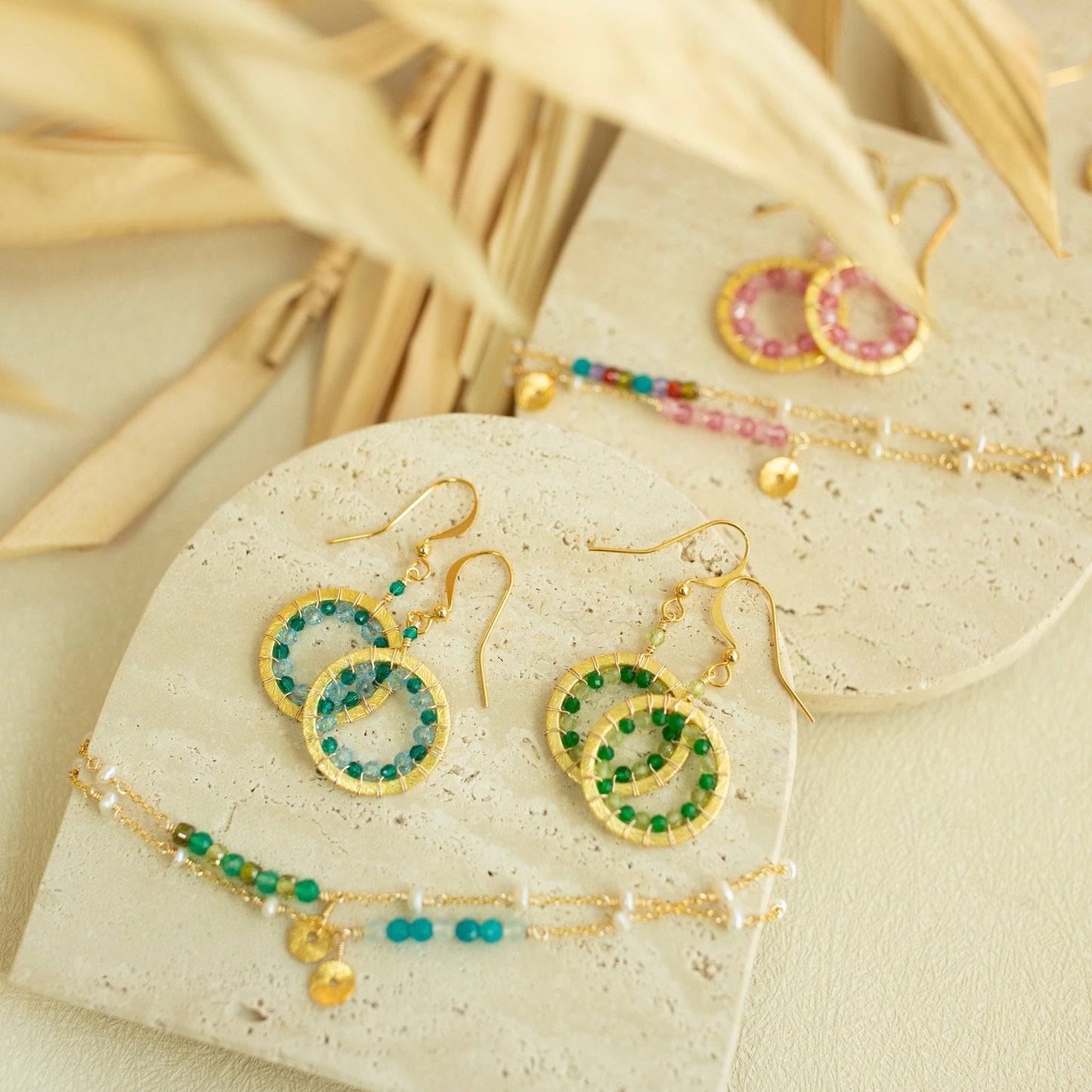 Jewelry set including earrings and a bracelet on a beige surface with dried leaves.