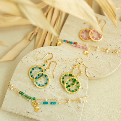 Jewelry set including earrings and a bracelet on a beige surface with dried leaves.