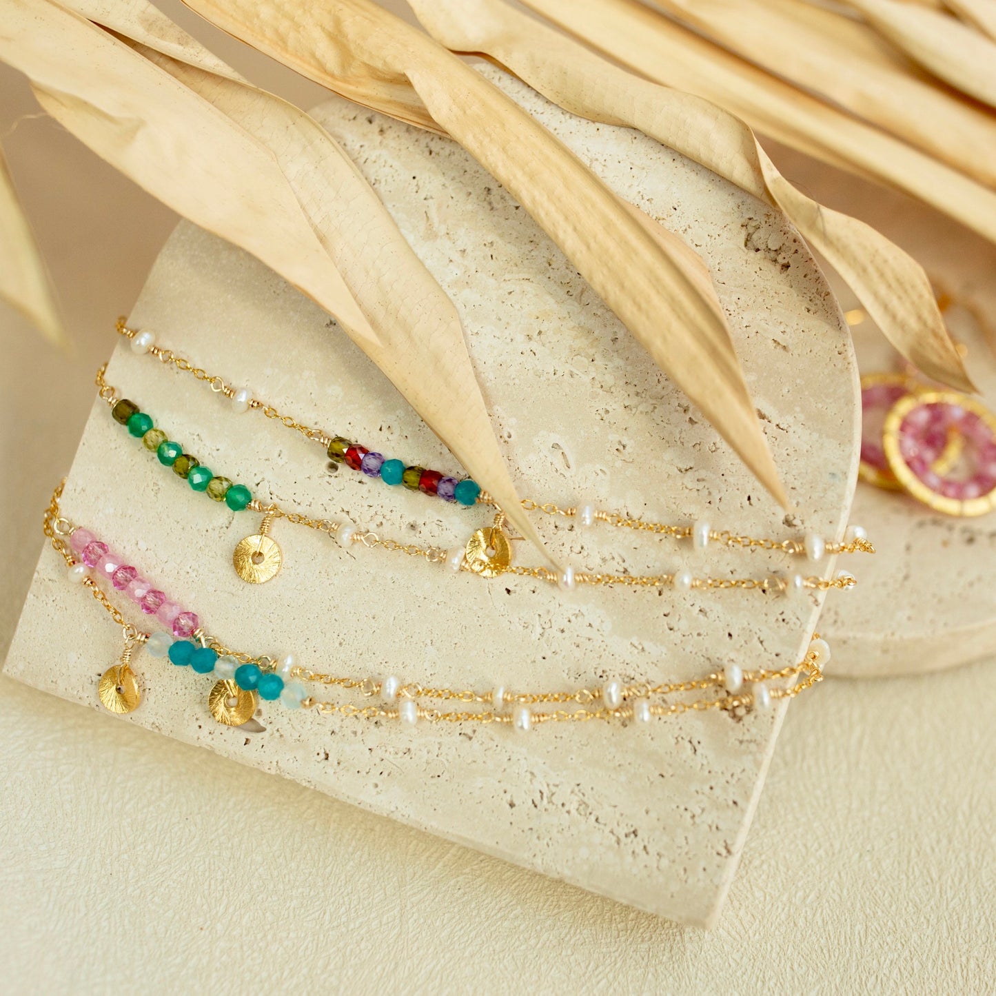 Set of gold bracelets with colorful beads on a textured surface with dried leaves.