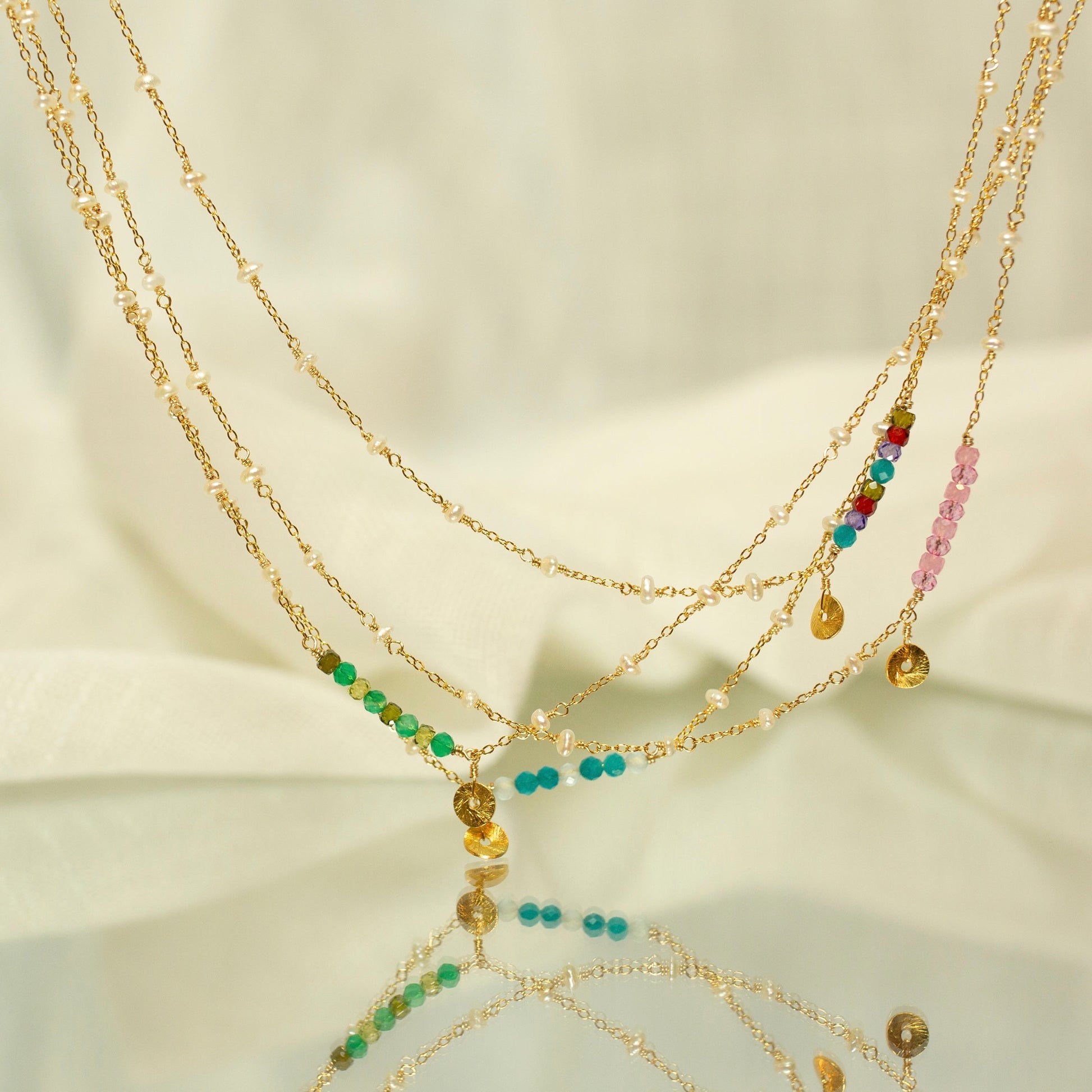 Multiple gold necklaces with colorful beads on a reflective surface