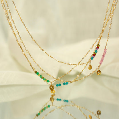 Multiple gold necklaces with colorful beads on a reflective surface