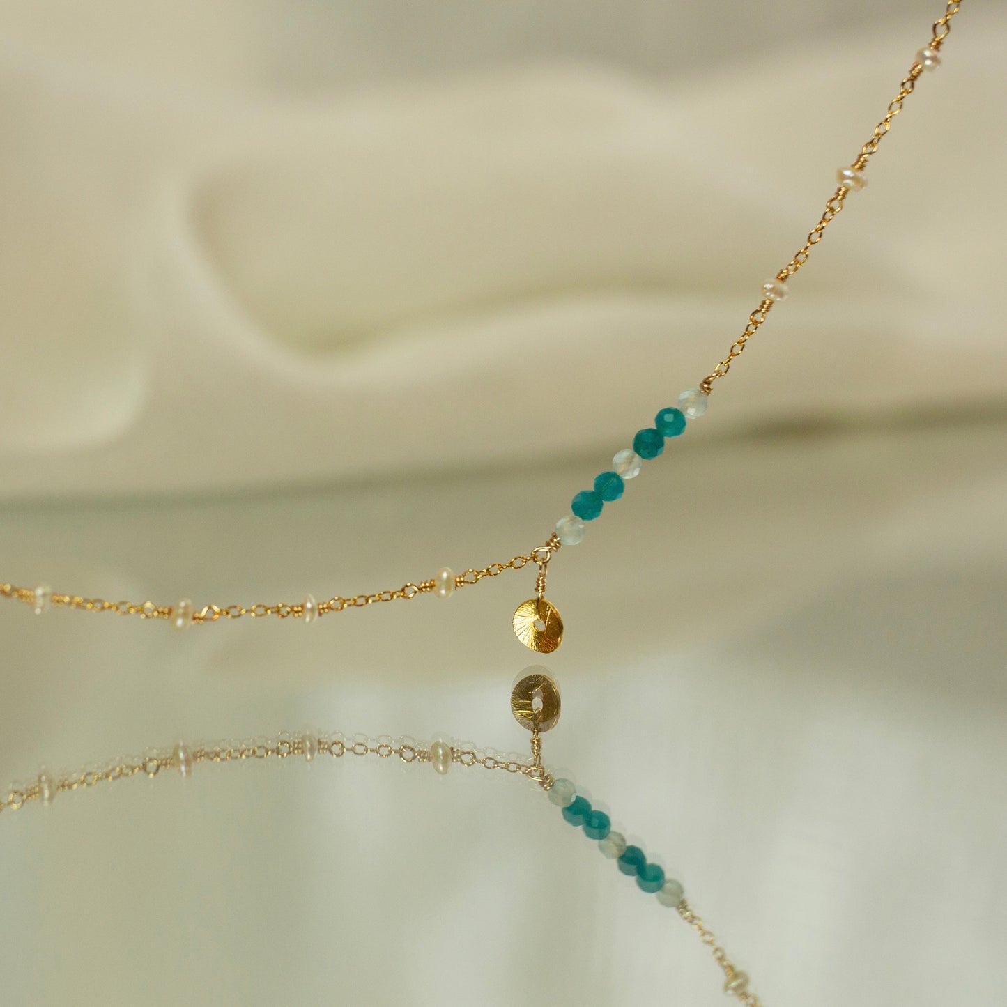 Delicate gold necklace with turquoise and white beads on a soft beige background