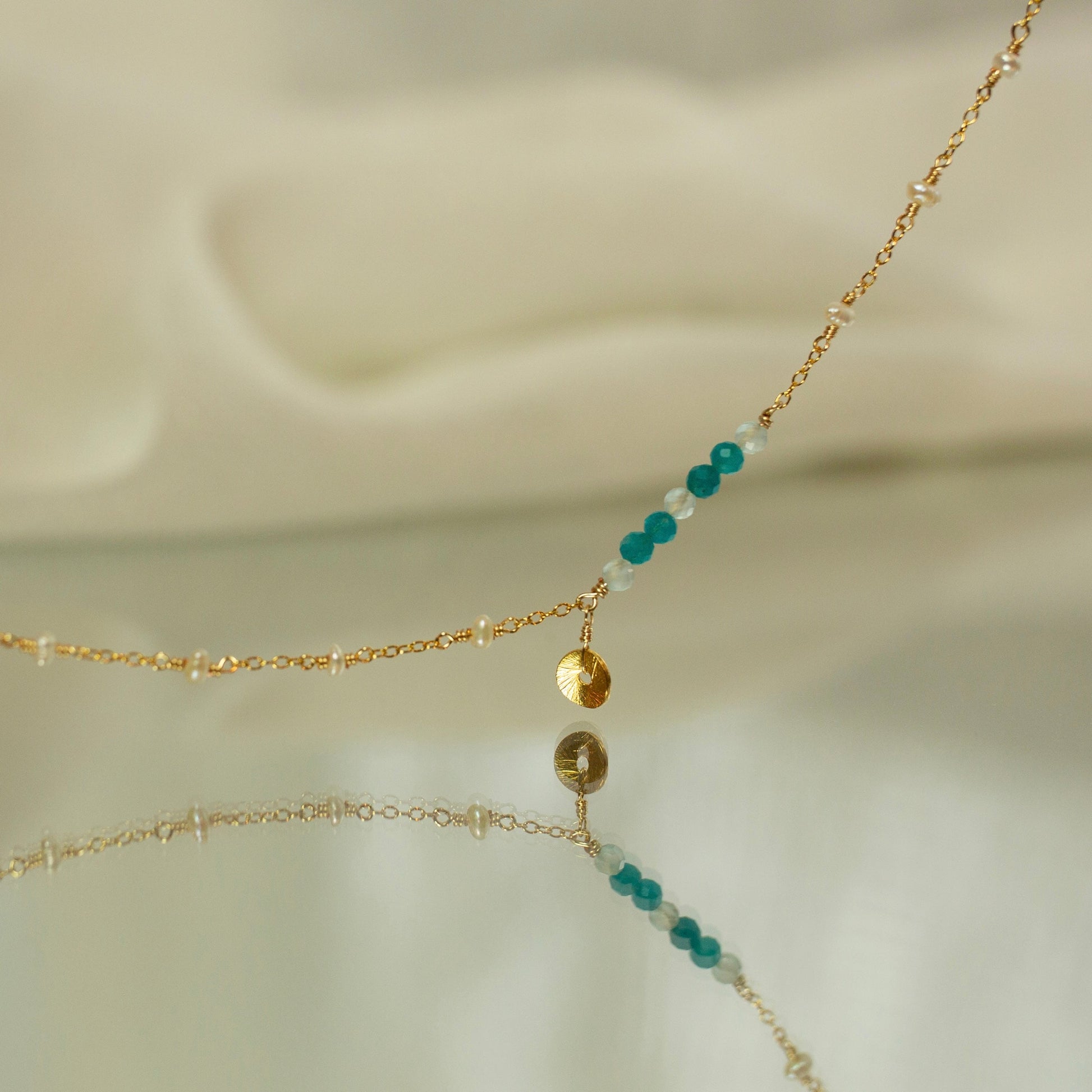Delicate gold necklace with turquoise and white beads on a soft beige background