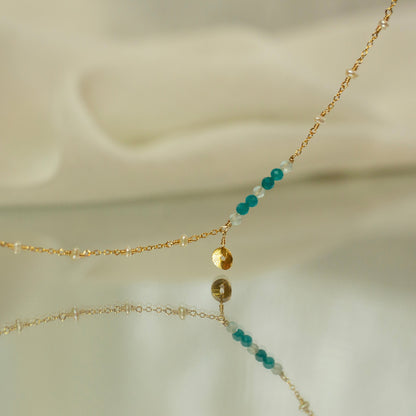 Delicate gold necklace with turquoise and white beads on a soft beige background