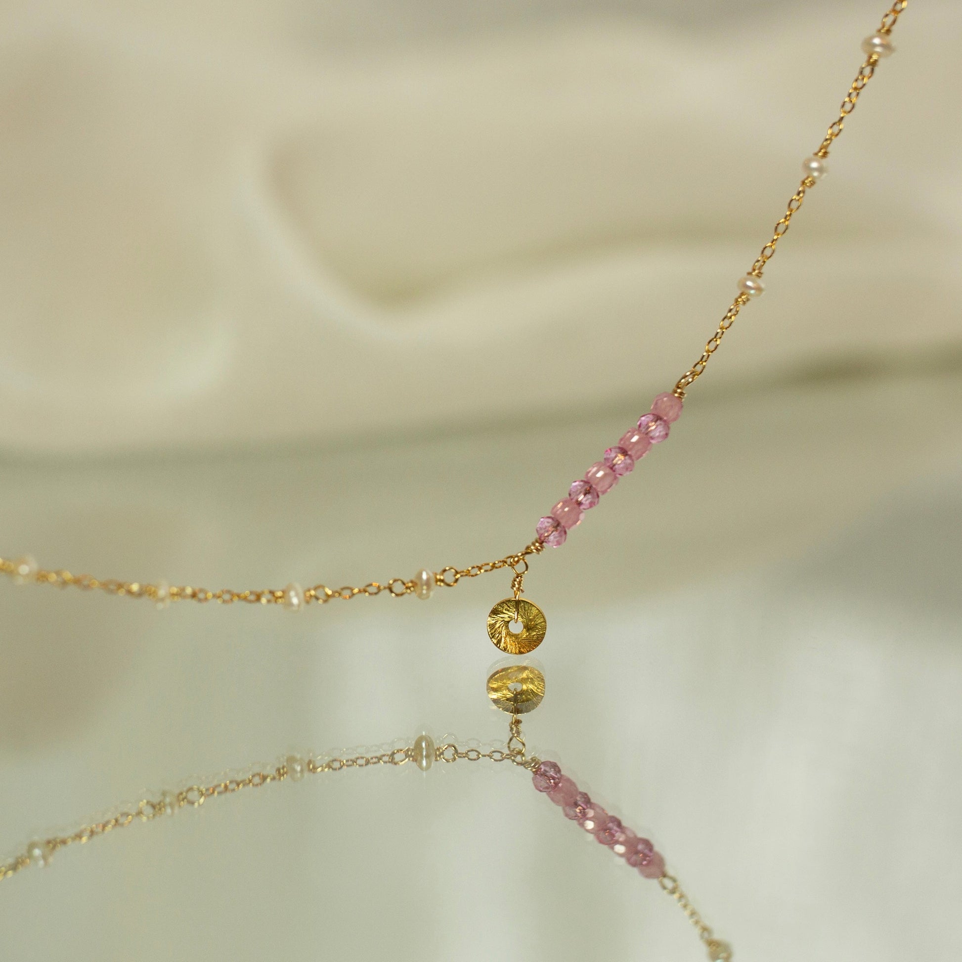 Delicate gold necklace with pink beads on a soft beige background