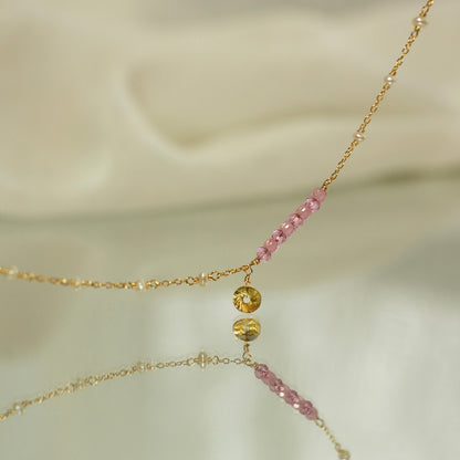 Delicate gold necklace with pink beads on a soft beige background