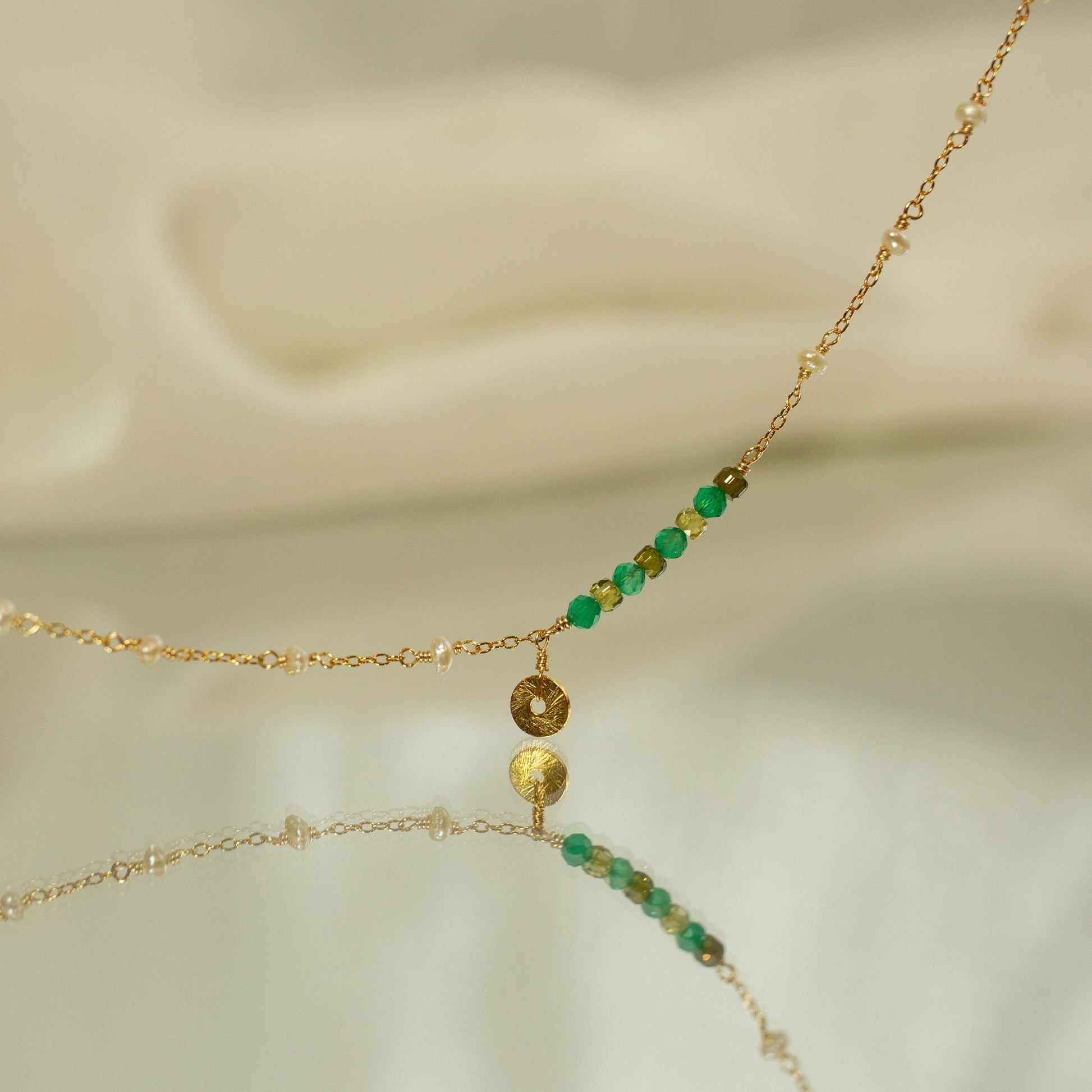 Gold and green beaded necklace on a soft beige background