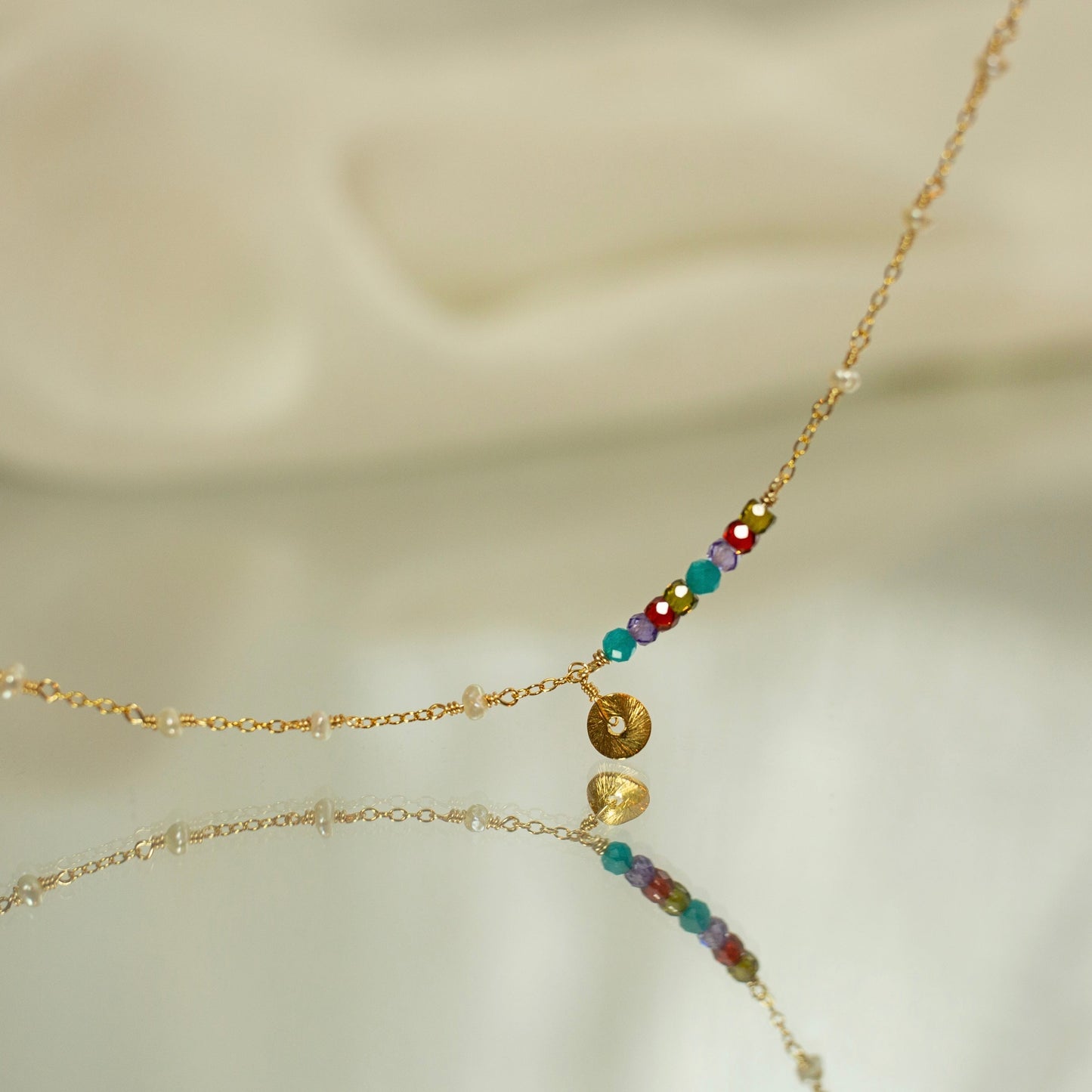 Delicate gold necklace with colorful beads on a soft beige background