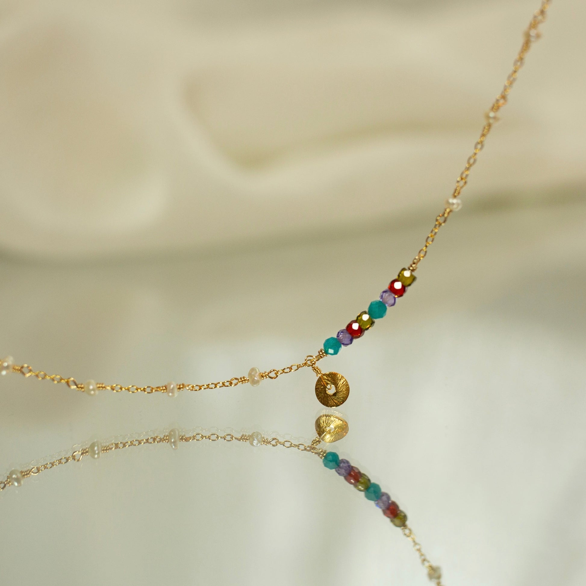 Delicate gold necklace with colorful beads on a soft beige background