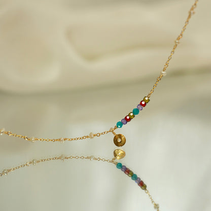Delicate gold necklace with colorful beads on a soft beige background