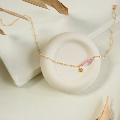 Gold bracelet with pink beads on a white marble surface
