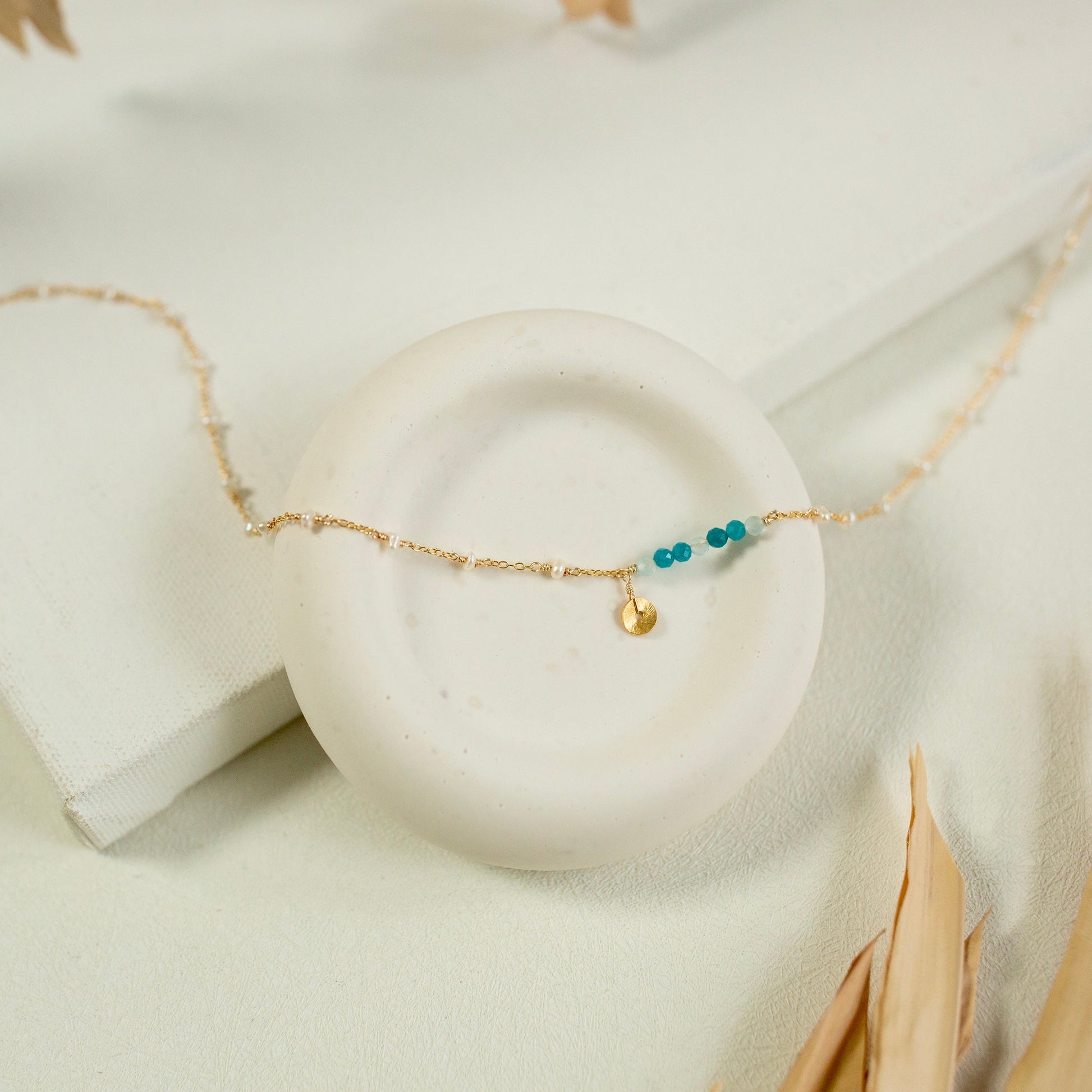 Gold bracelet with turquoise beads on a white stone surface
