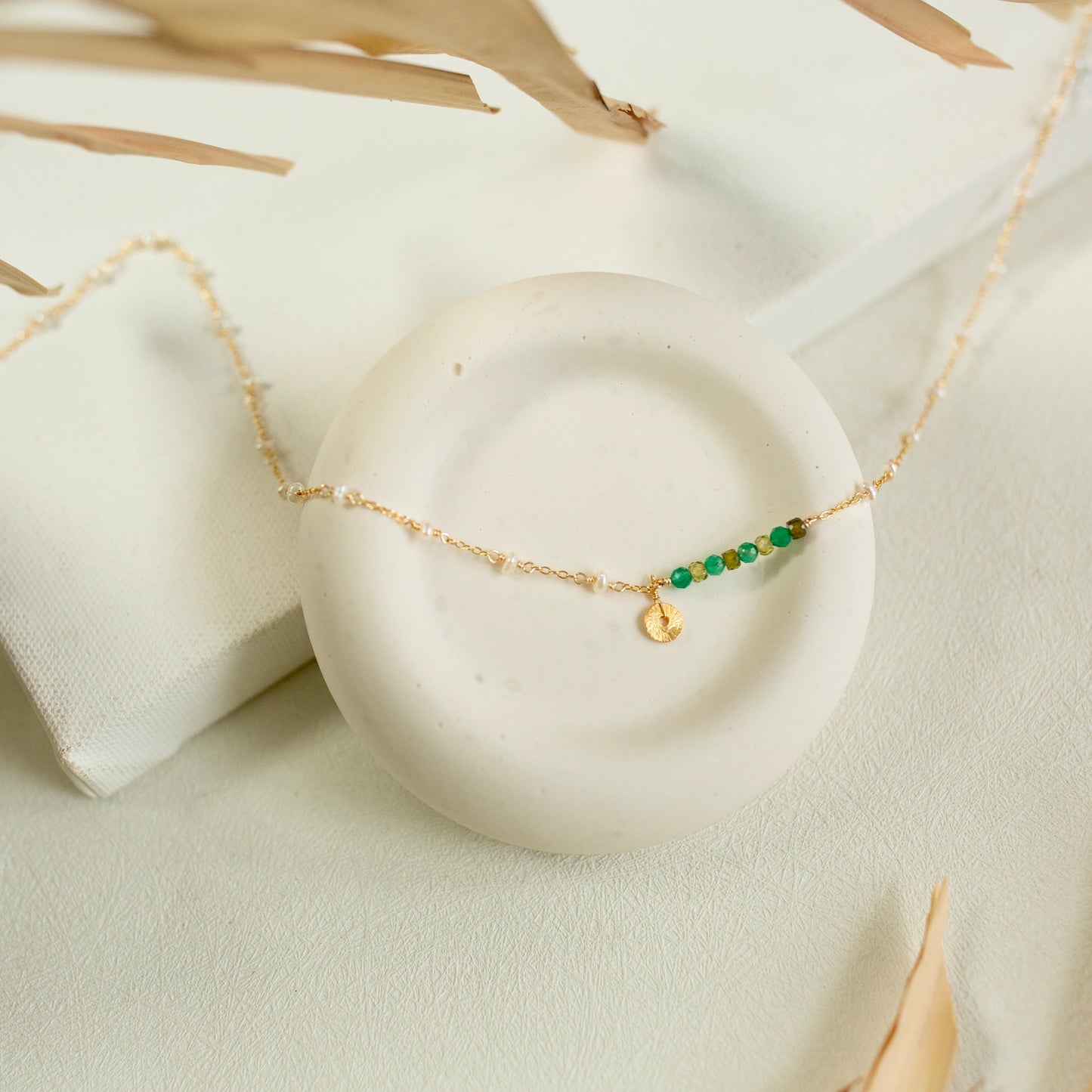 Gold necklace with green beads on a white stone surface