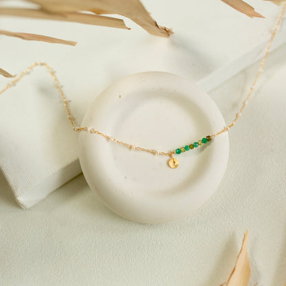 Gold necklace with green beads on a white stone surface