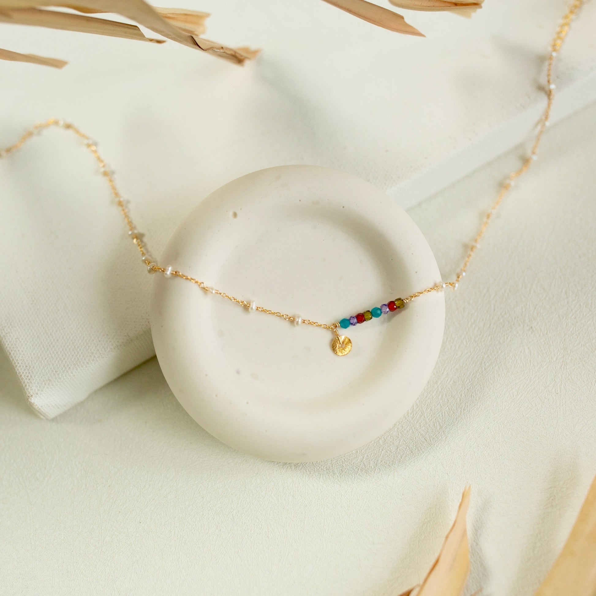 Gold necklace with colorful beads on a white stone surface
