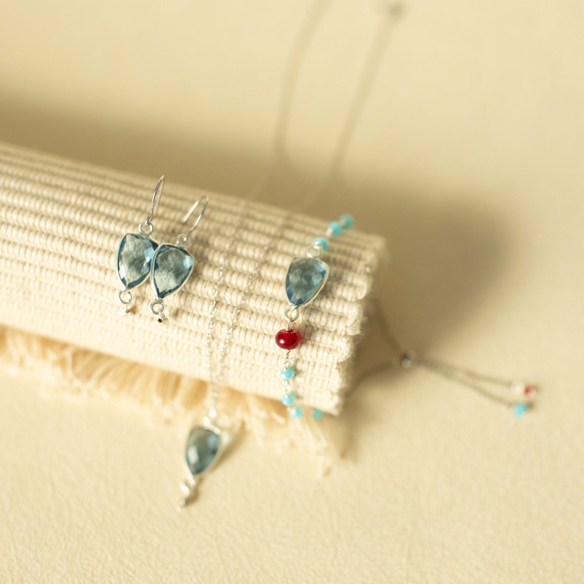 Pair of earrings with blue teardrop-shaped stones on a beige fabric background