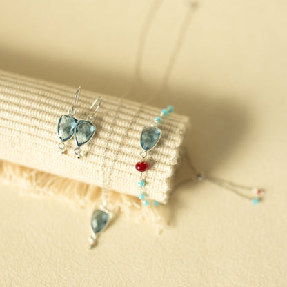 Pair of earrings with blue teardrop-shaped stones on a beige fabric background