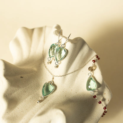 Green leaf-shaped earrings on a beige starfish