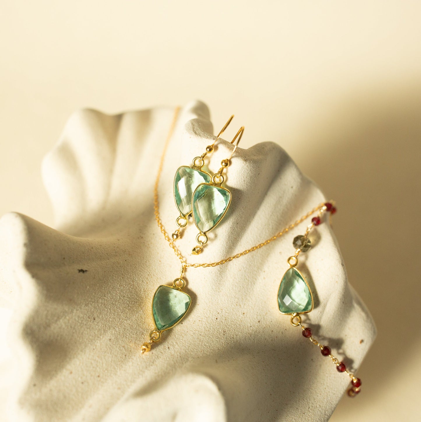 Gold earrings with green heart-shaped stones on a beige background