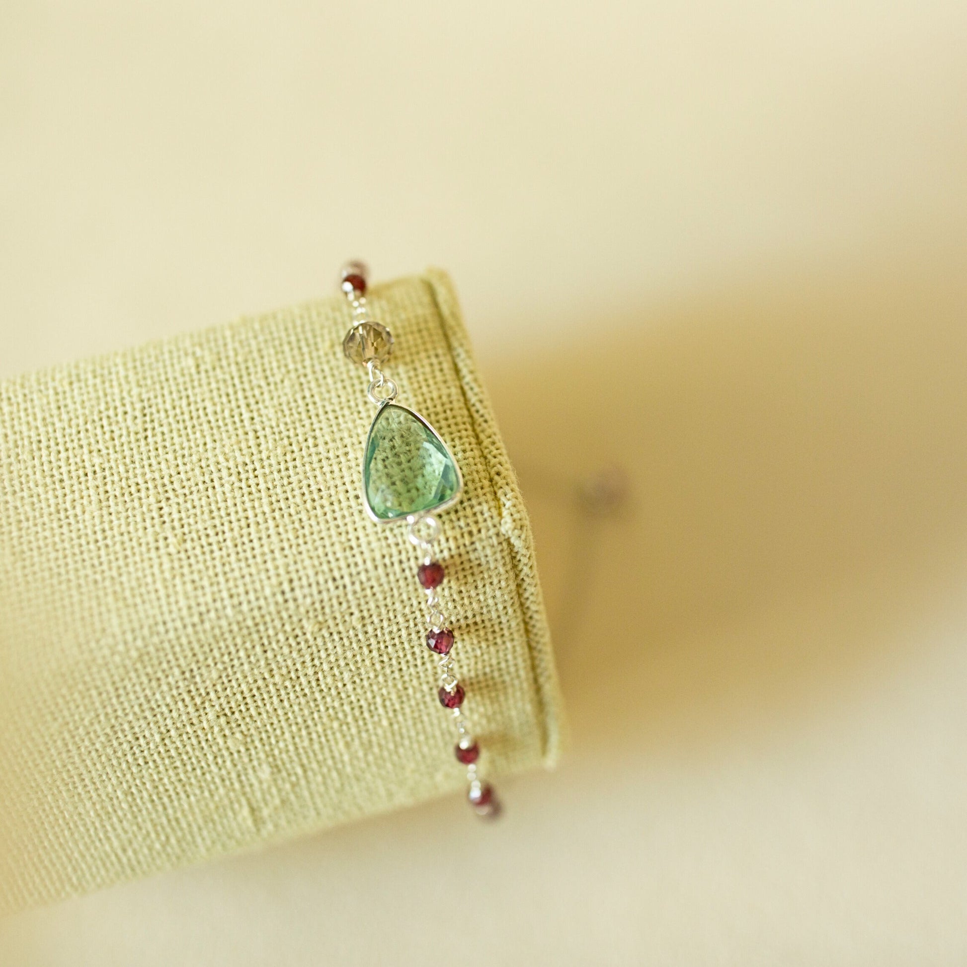 Bracelet with a green gemstone and red beads on a beige fabric background
