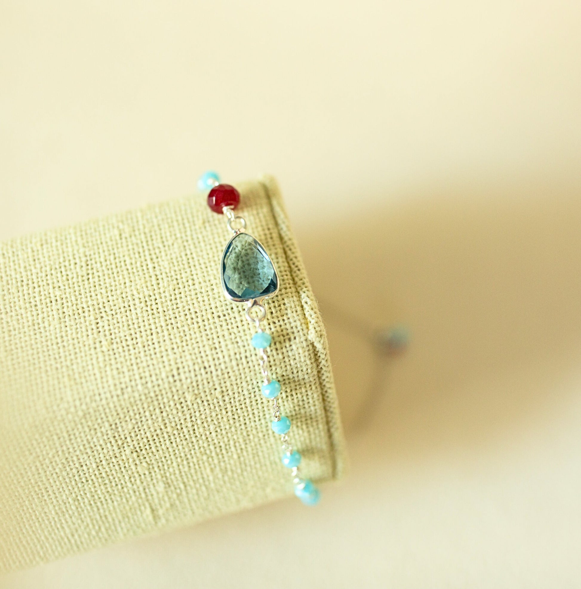 Jewelry with a central blue stone and smaller beads on a beige fabric background
