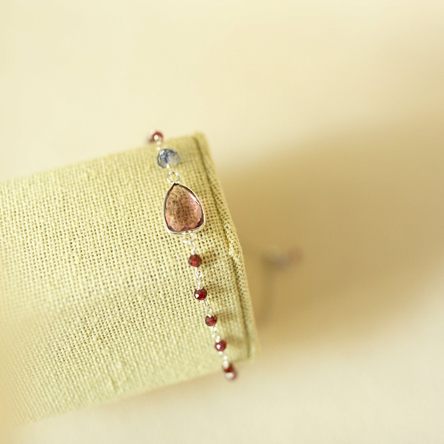 Bracelet with teardrop-shaped charm and red beads on a beige background