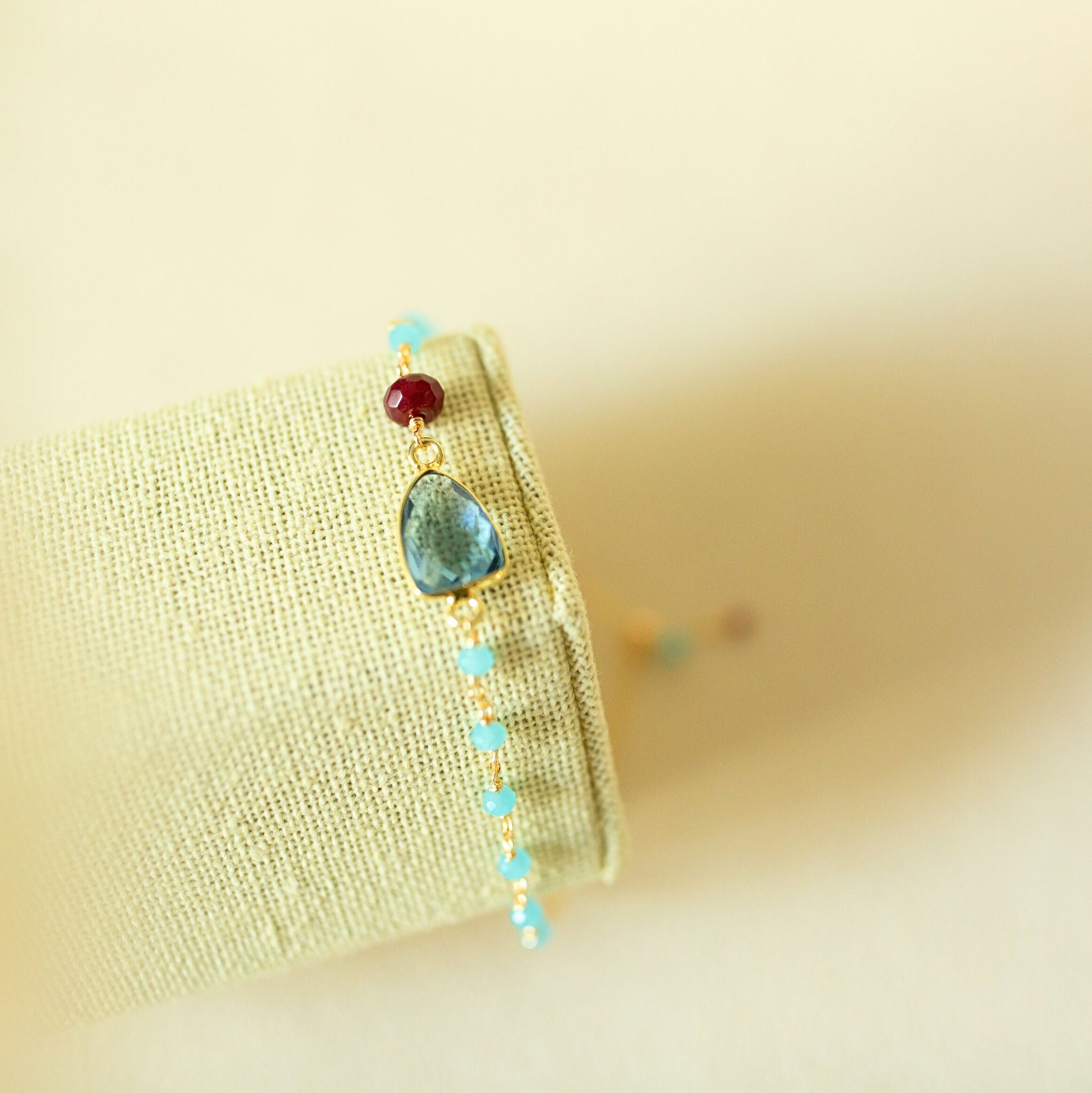 Bracelet with turquoise stones and a red gemstone on a beige fabric background
