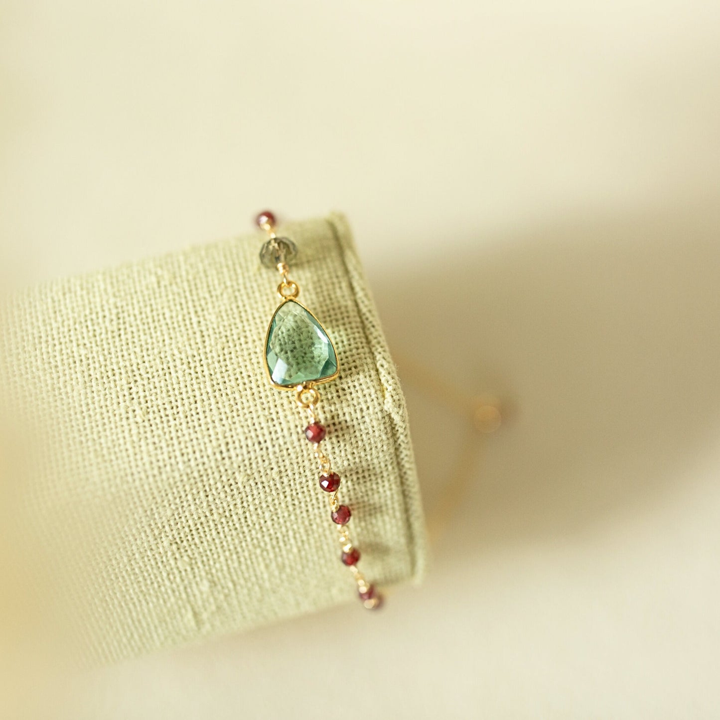Bracelet with green teardrop charm and red beads on a light fabric background