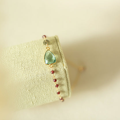 Bracelet with green teardrop charm and red beads on a light fabric background