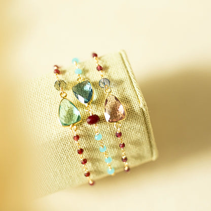 Colorful earrings with gemstones on a textured beige background