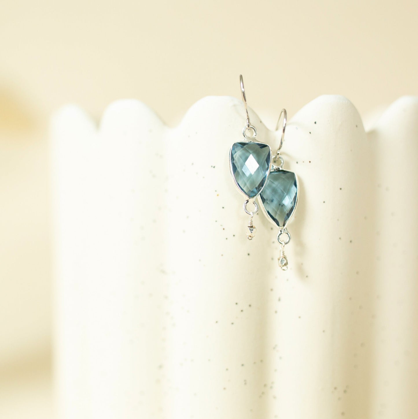 Pair of heart-shaped blue gemstone earrings on a white stand.