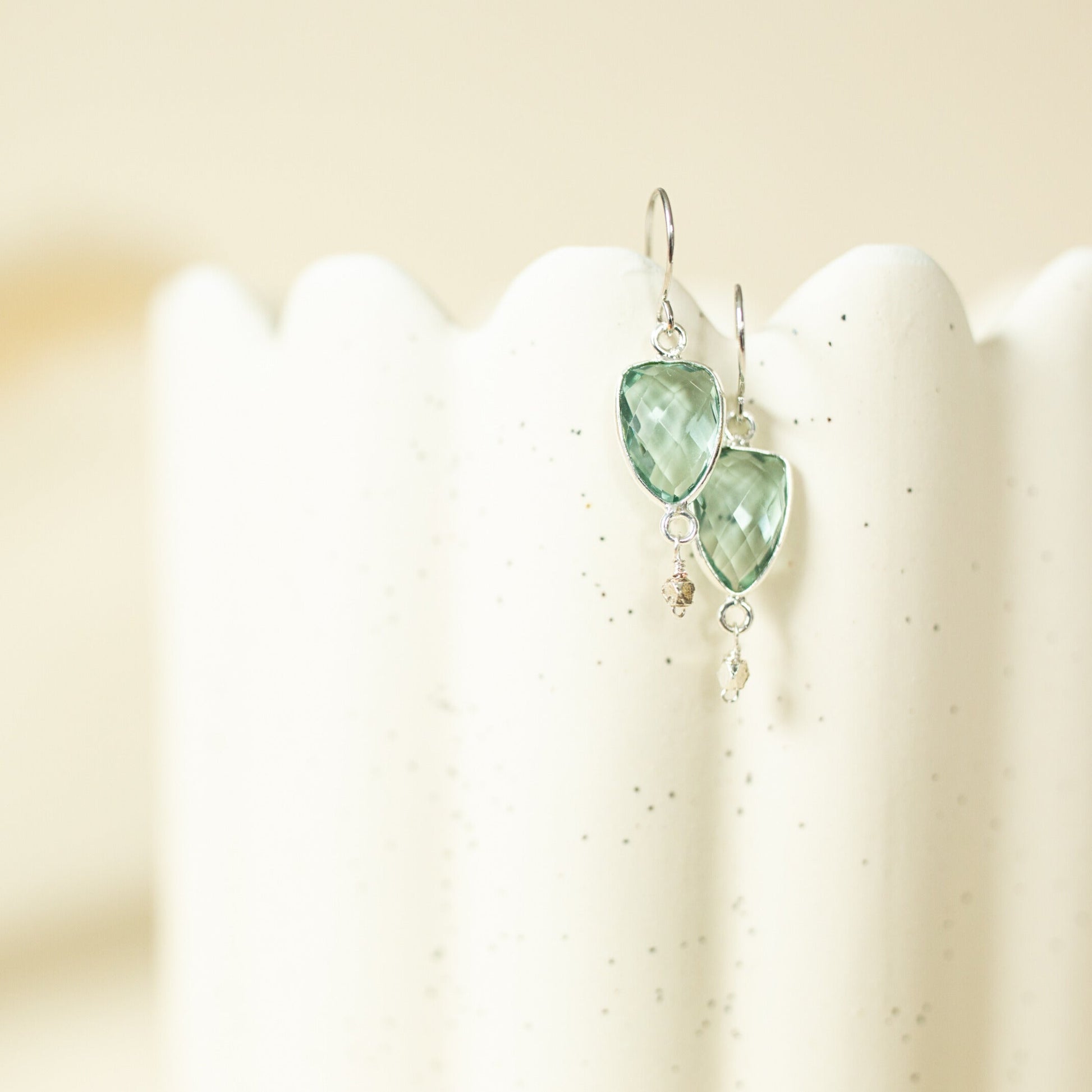 Green teardrop earrings on a white stand with a beige background
