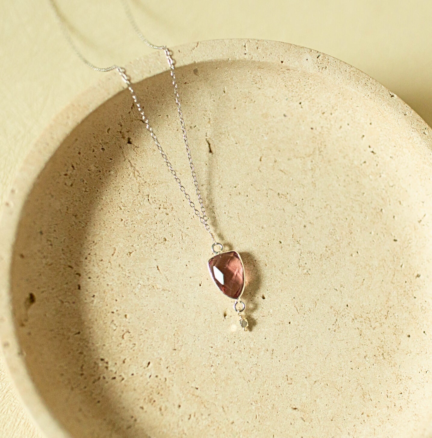Necklace with a pink pendant on a beige stone surface