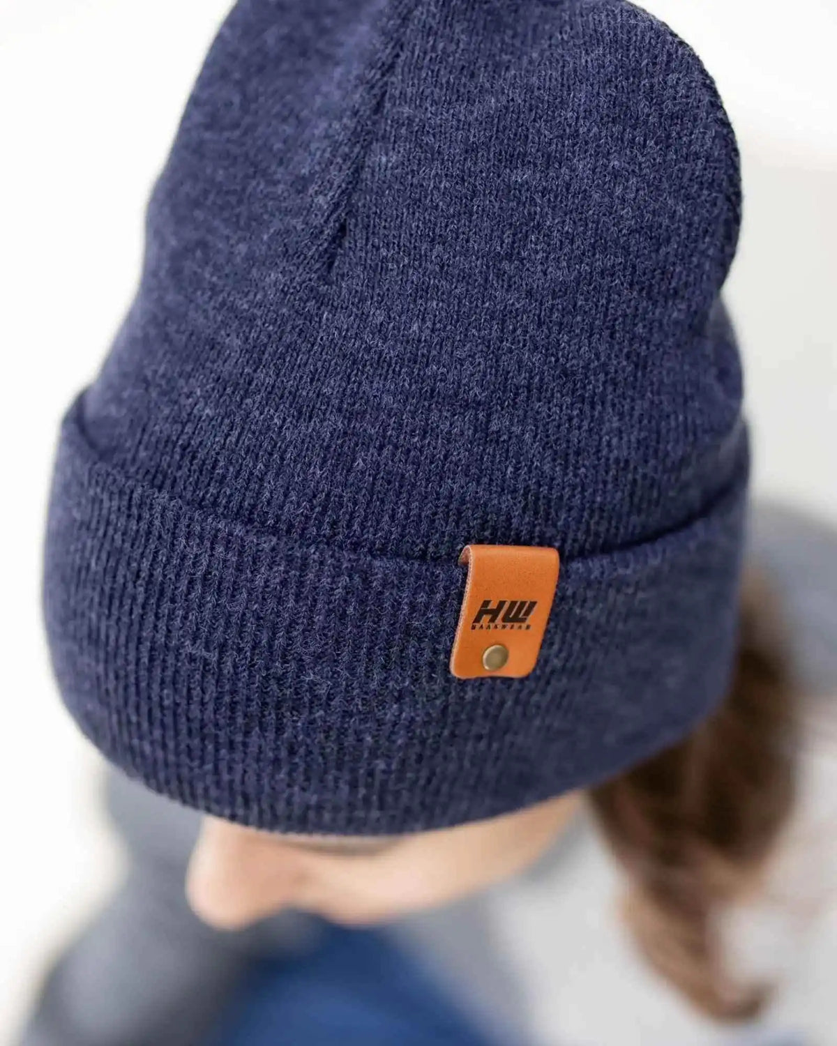 Navy blue knit beanie with a brown leather patch on a blurred background
