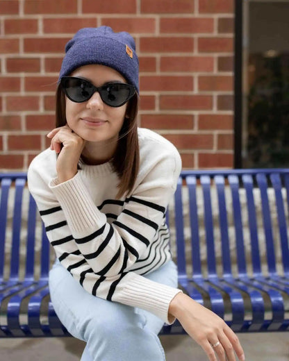 Woman wearing a striped sweater and sunglasses sitting on a blue bench against a brick wall.