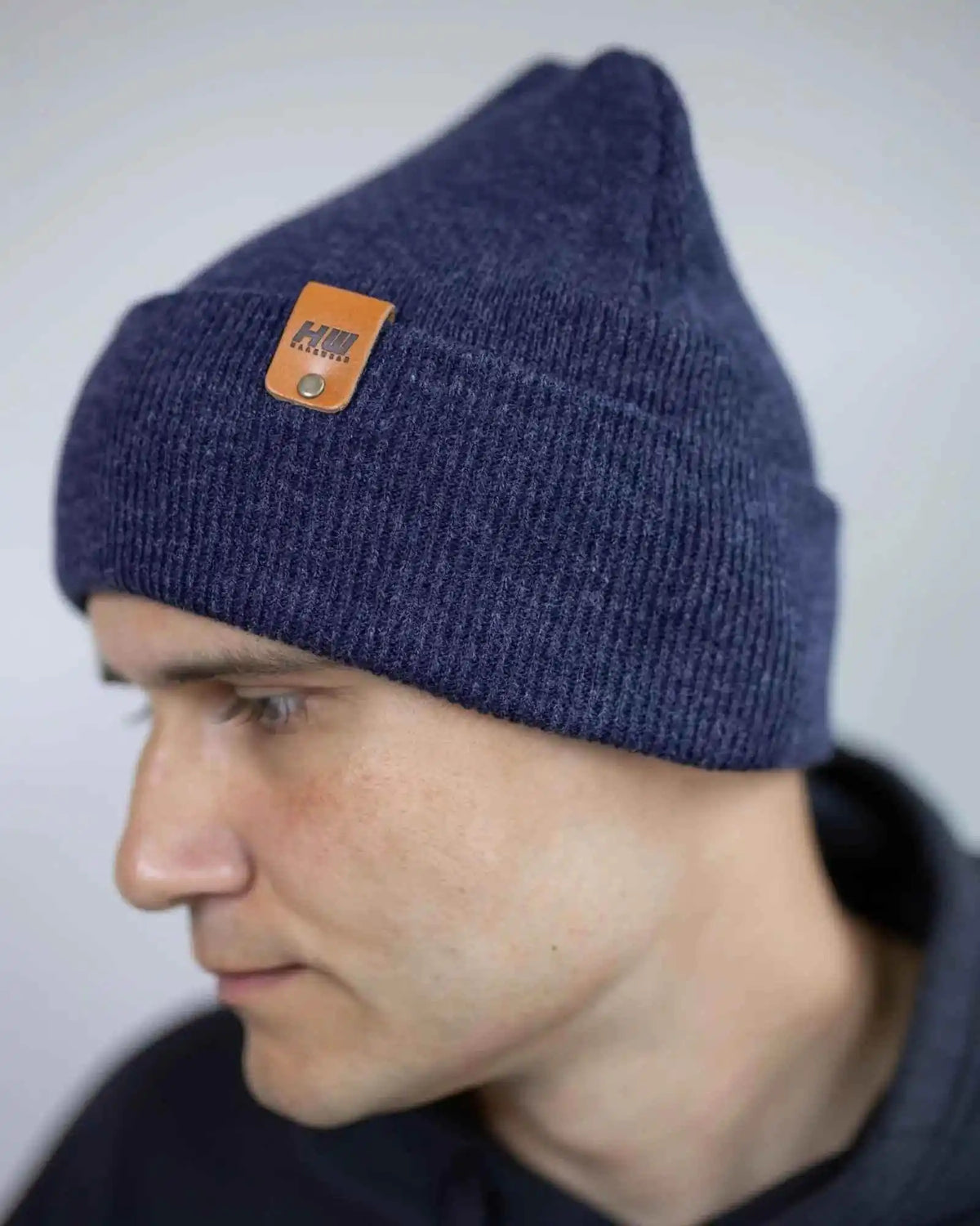 Person wearing a blue knit beanie with a brand logo on a plain background