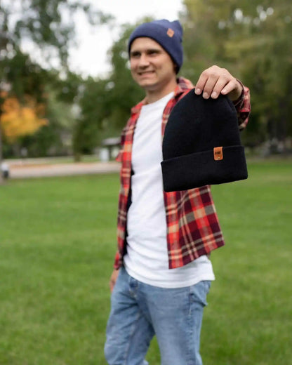 Person holding a black beanie outdoors on a grassy area