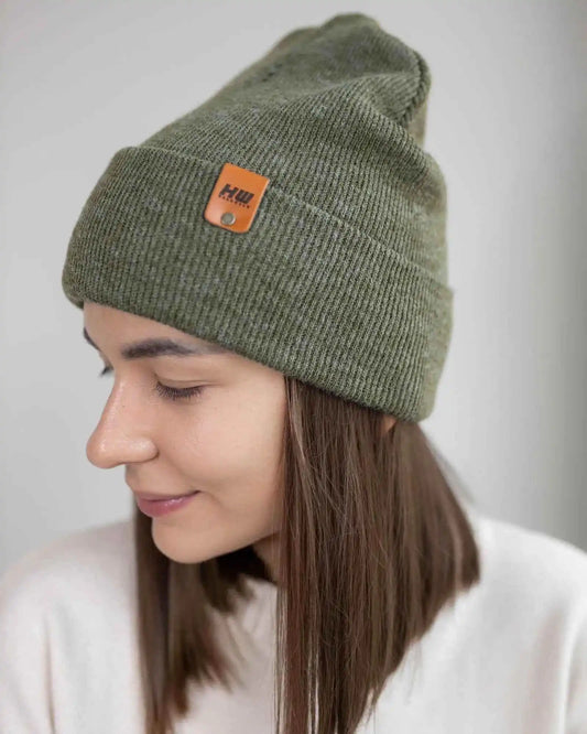 Person wearing a green beanie with a brand logo on a plain background