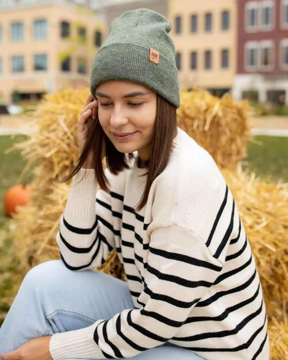 Woman wearing a striped sweater and green beanie sitting on hay bales with pumpkins in the background