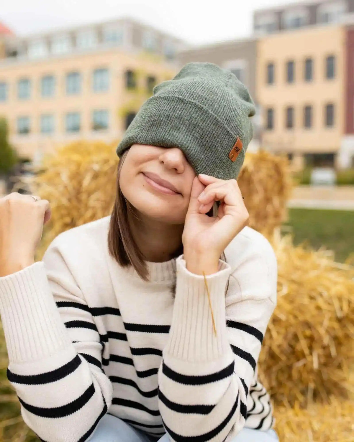 Person wearing a green beanie and striped sweater outdoors with blurred buildings in the background