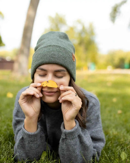 Person wearing a green beanie and gray sweater holding a leaf in a park