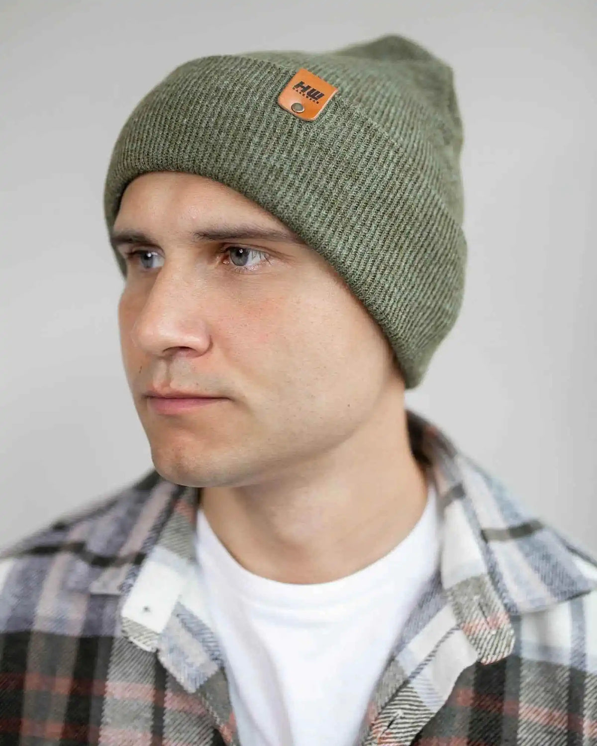 Man wearing a green beanie with a brand logo against a plain background