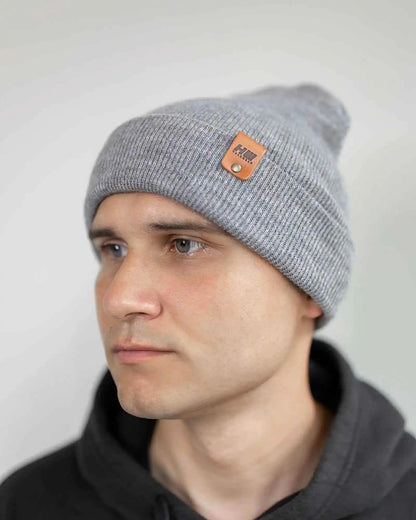 Person wearing a gray beanie with a brand logo on a plain background