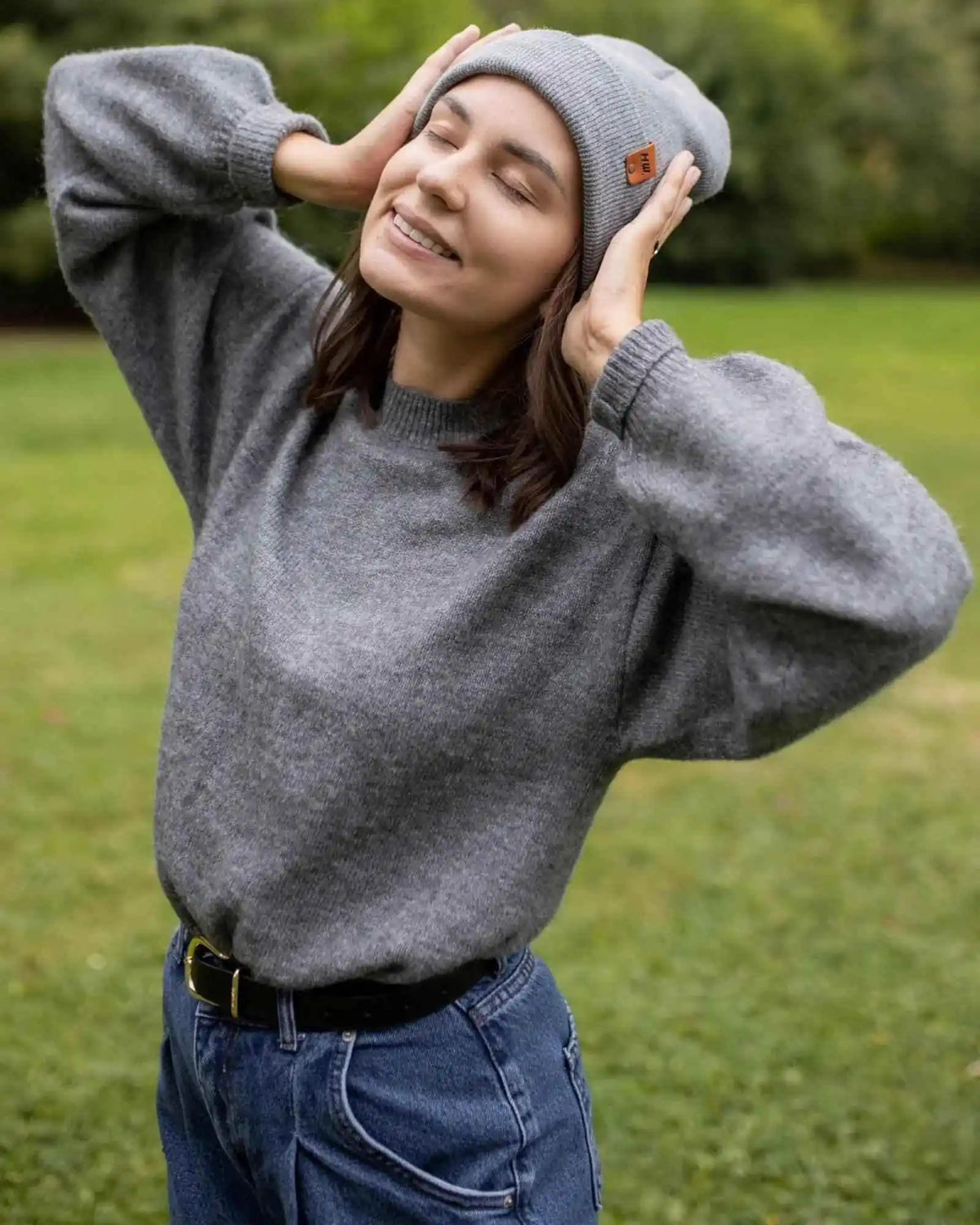 Person wearing a gray sweater and beanie outdoors on a grassy area
