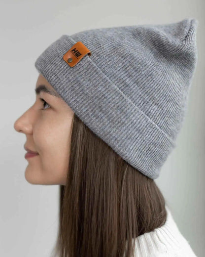 Person wearing a gray beanie with a brand logo on a plain background