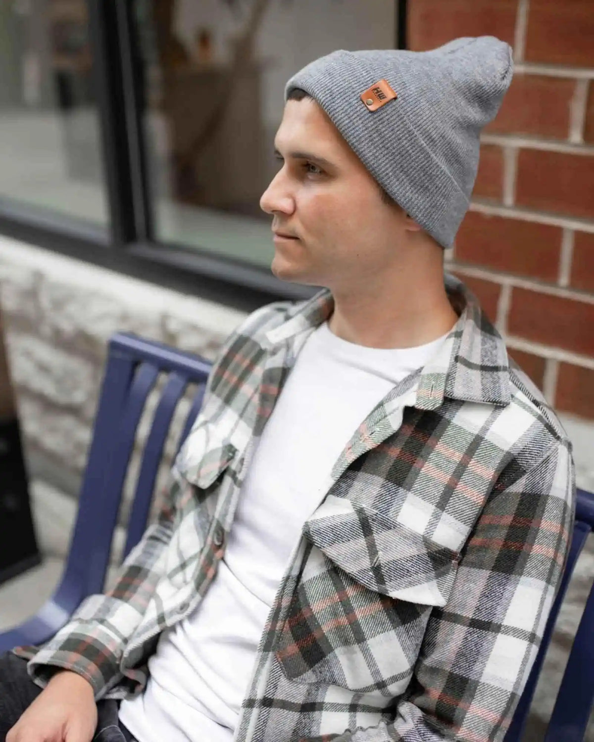 Person wearing a gray beanie and plaid shirt sitting outdoors.