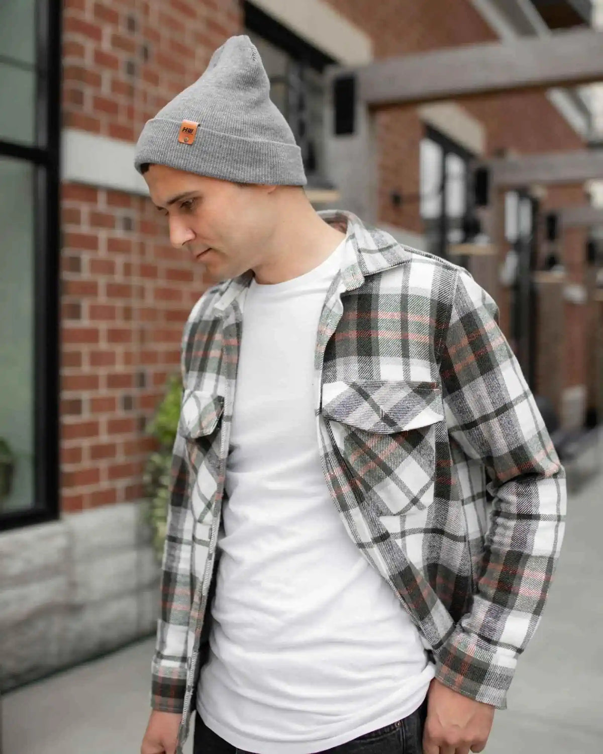 Man wearing a gray beanie and plaid shirt over a white t-shirt outdoors.