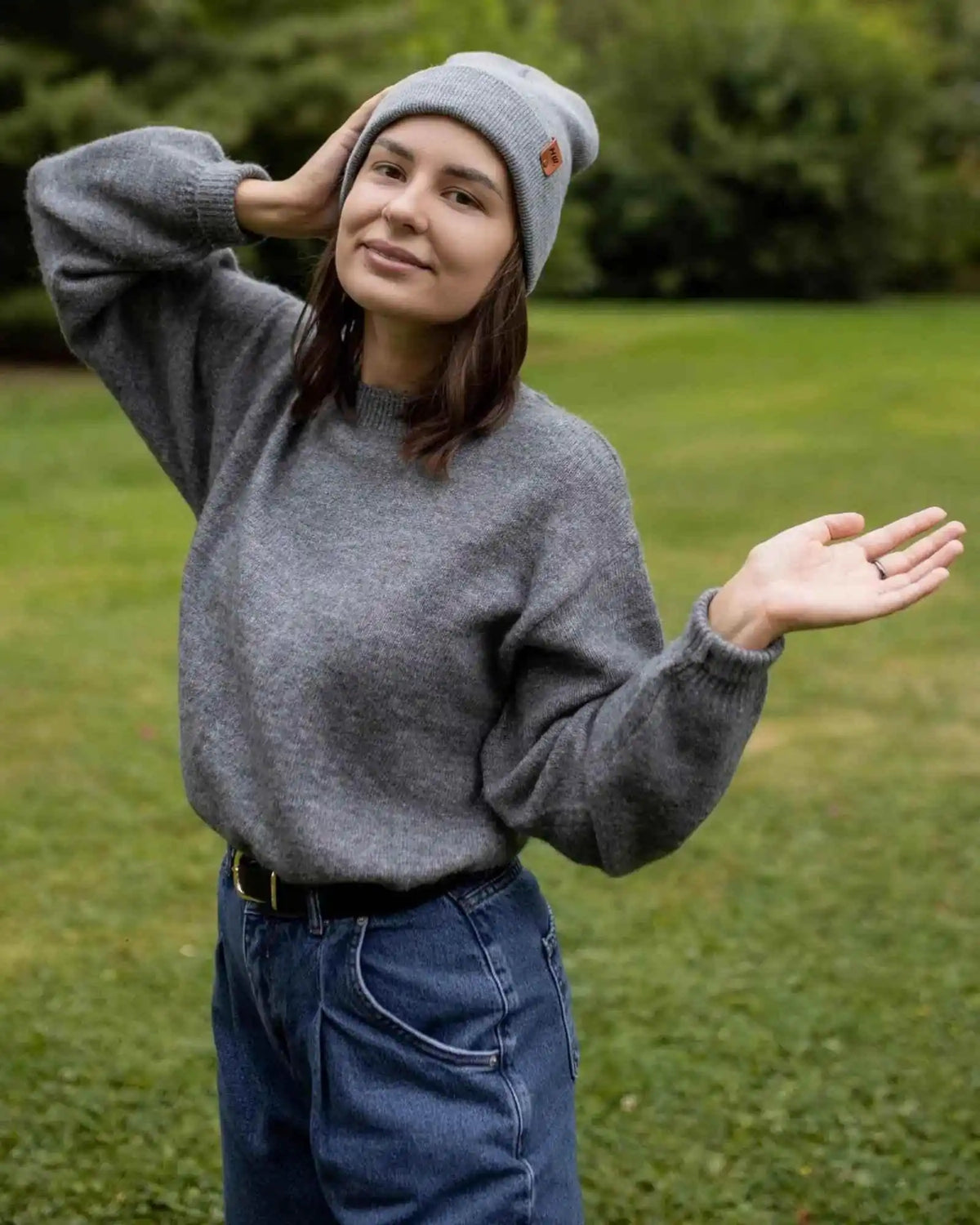 Woman wearing a gray sweater and beanie outdoors on a grassy area