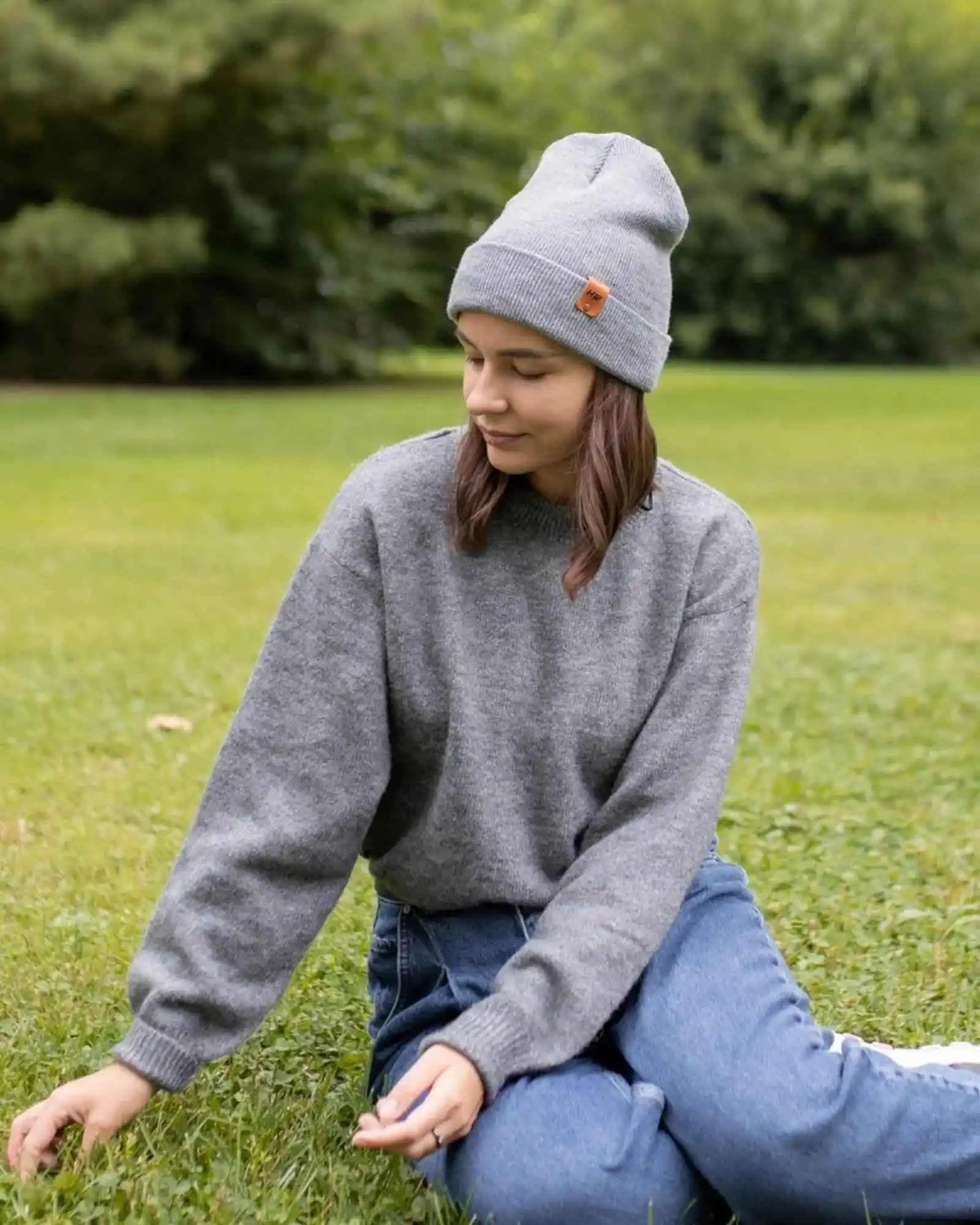Person wearing a gray sweater and beanie sitting on grass