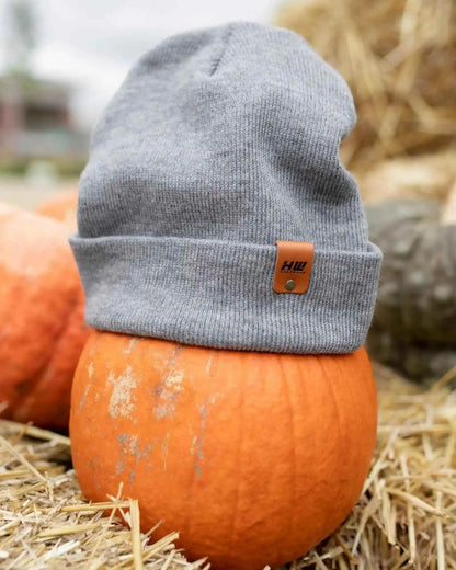 Gray beanie with a brown tag on an orange pumpkin surrounded by hay.